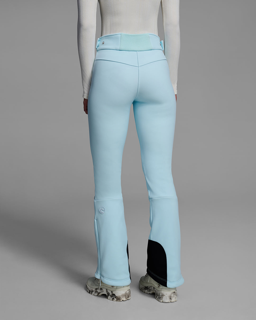 Back detail view of a woman wearing a 4-way stretch ski pant in iceberg blue and a white base layer top. #color_iceberg