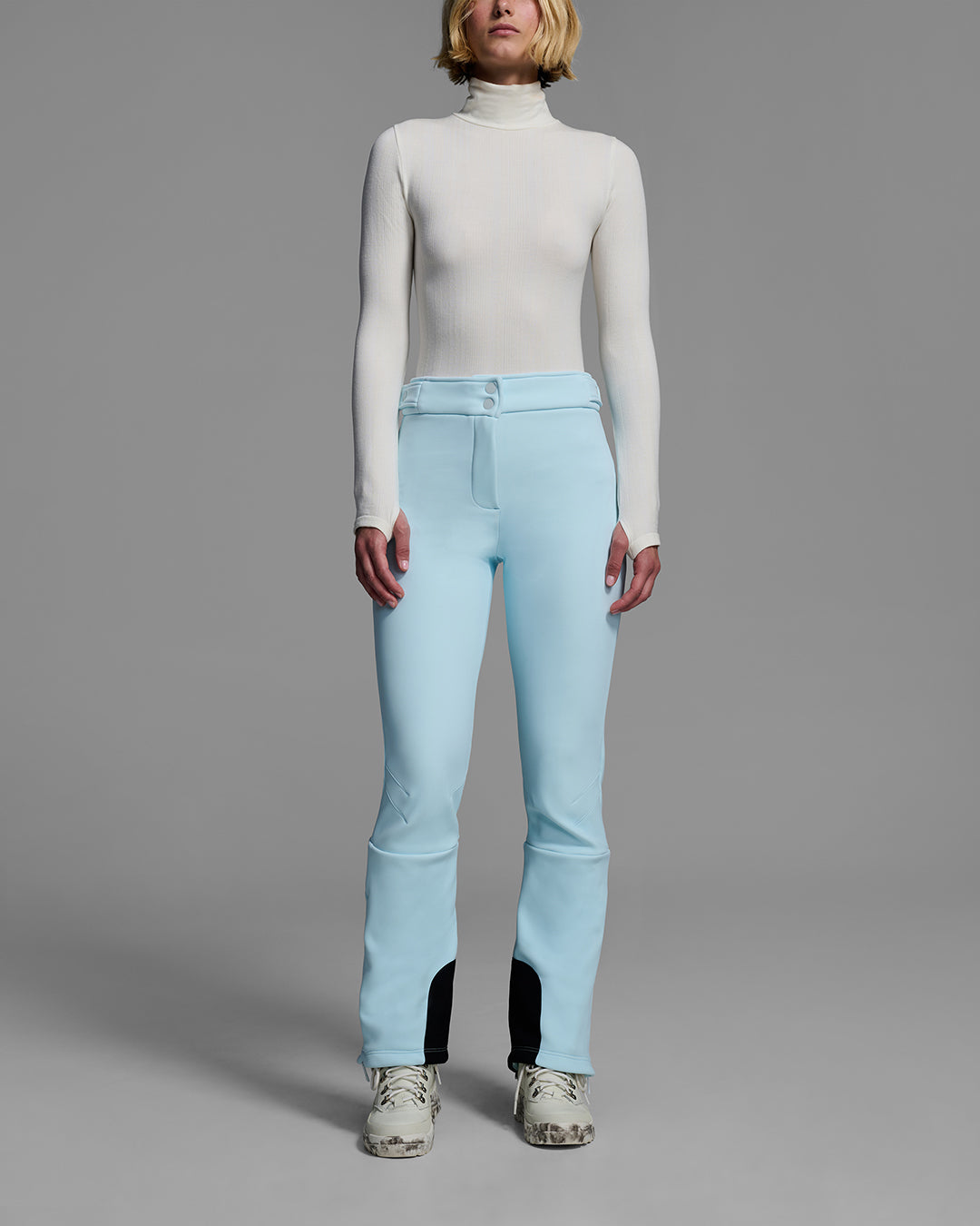 Detail front view of a woman wearing a 4-way stretch ski pant in iceberg blue and a white base layer top. #color_iceberg