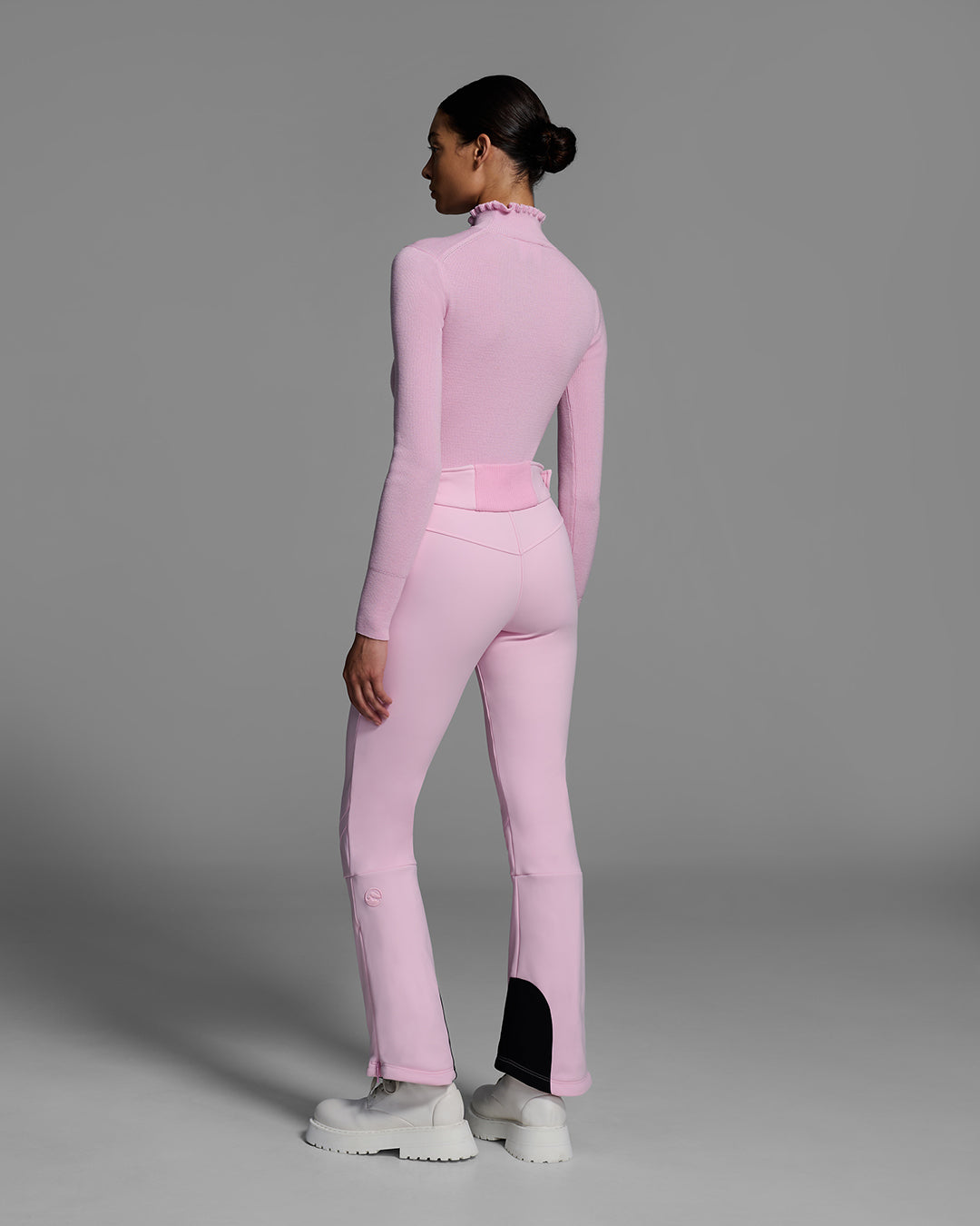 Back view of a woman wearing a 4-way stretch ski pant in peony pink and a matching base layer top. #color_peony
