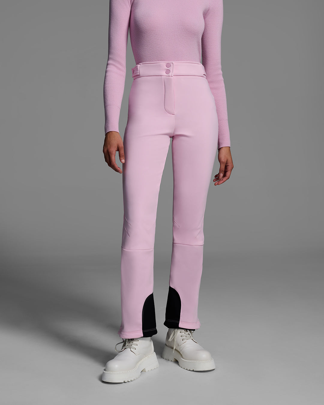 Detail front view of a woman wearing a 4-way stretch ski pant in peony pink and a matching base layer top. #color_peony