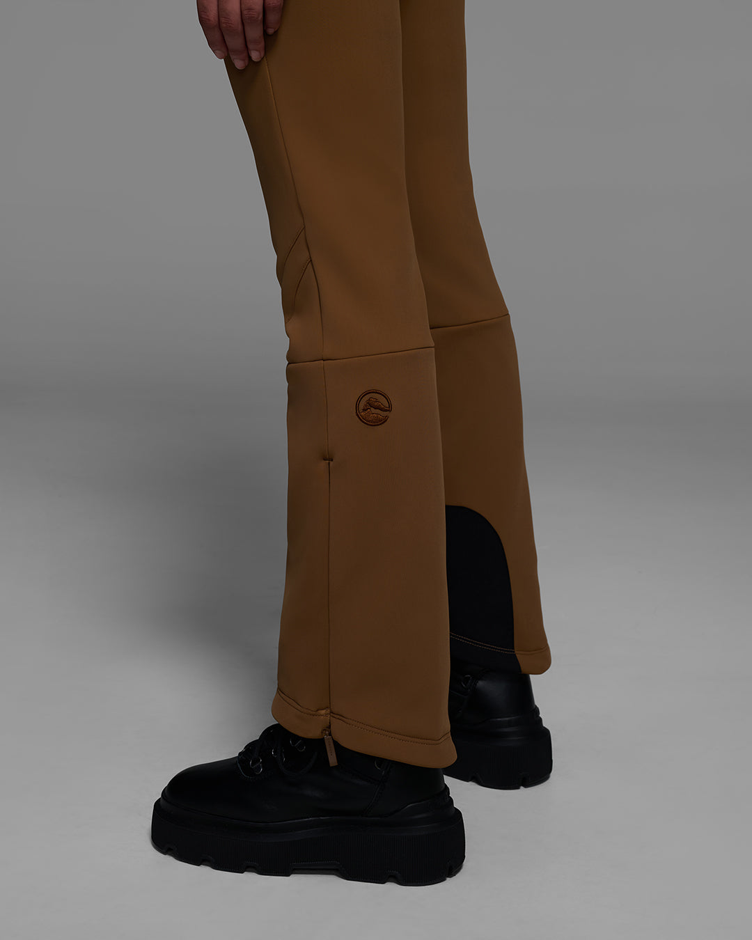 Detail view of the leg of a 4-way stretch ski pant in sepia brown with a logo on the leg. #color_sepia