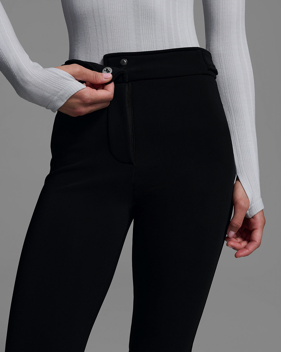 Detail shot of the t-snap of a black ski pant on Woman with a gray base layer top. #color_onyx