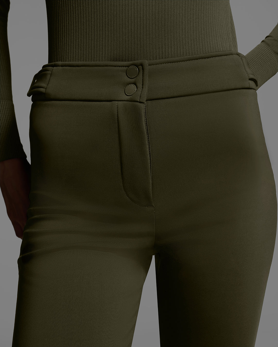 Close up detail of the fly of the pant of a woman wearing a 4-way stretch ski pant in khaki green with a matching base layer top. #color_khaki