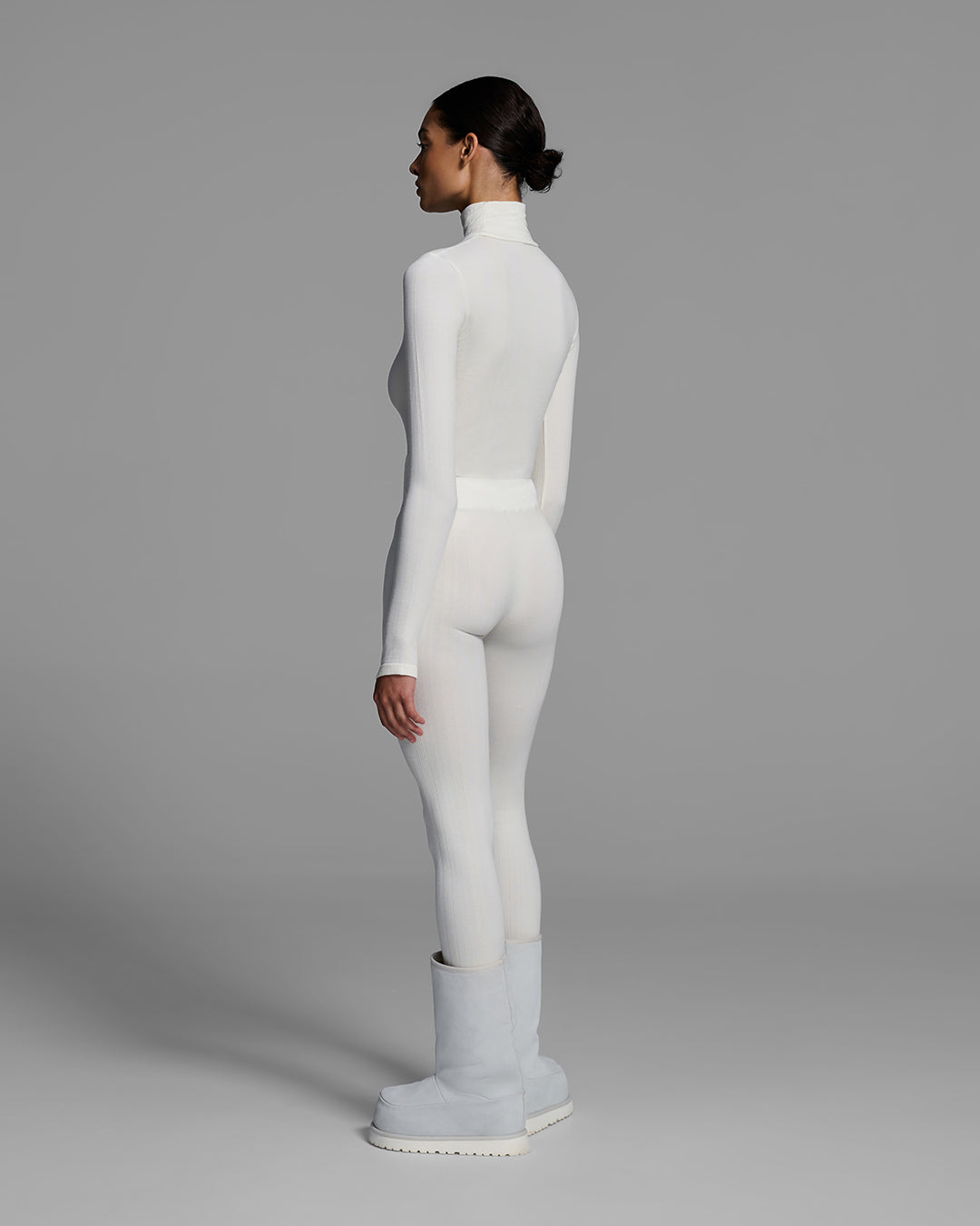 Back view of a woman wearing a white turtleneck and matching pant base layer set made of merino wool blend. #color_alabaster