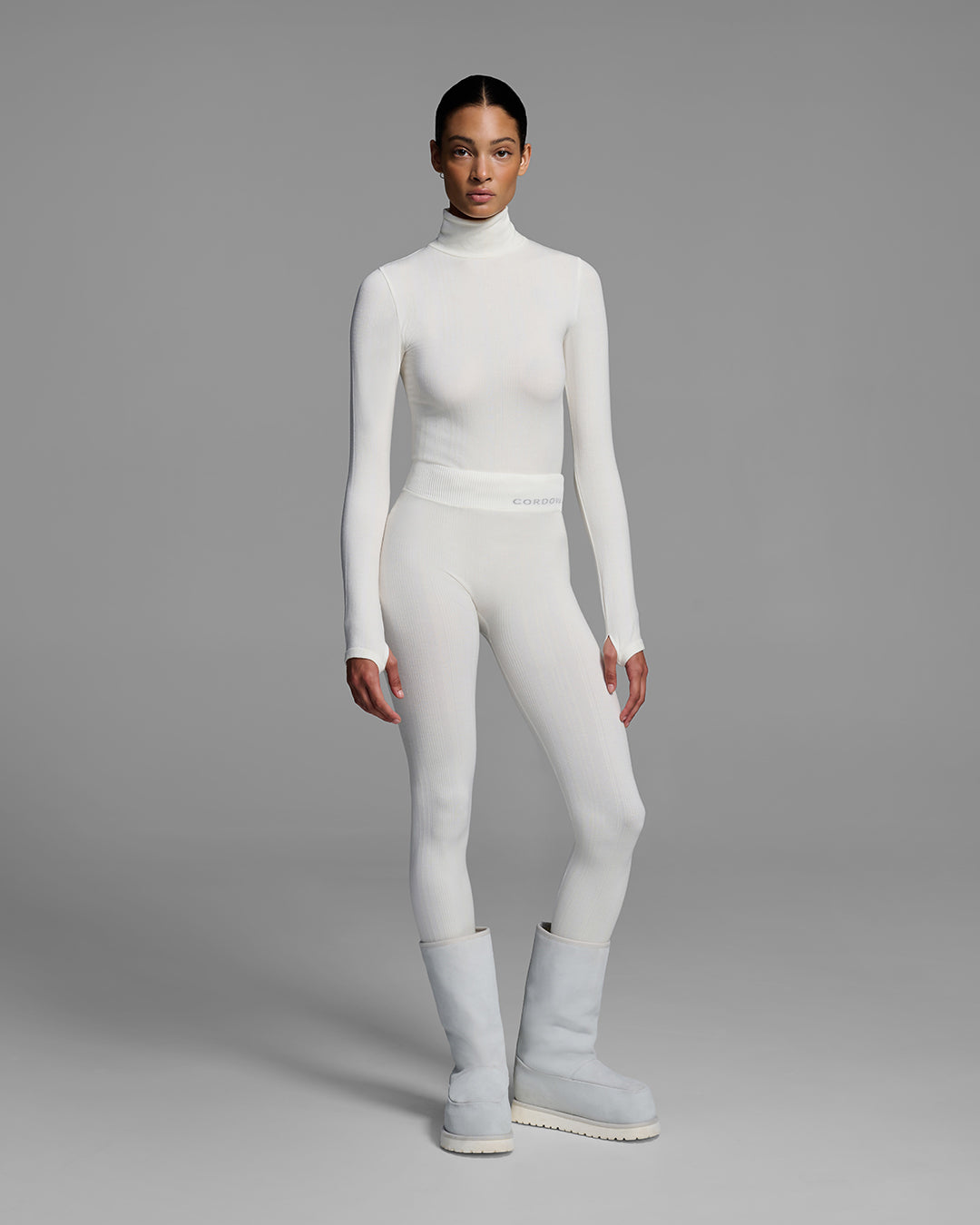 Woman wearing a white turtleneck and matching pant base layer set made of merino wool blend. #color_alabaster