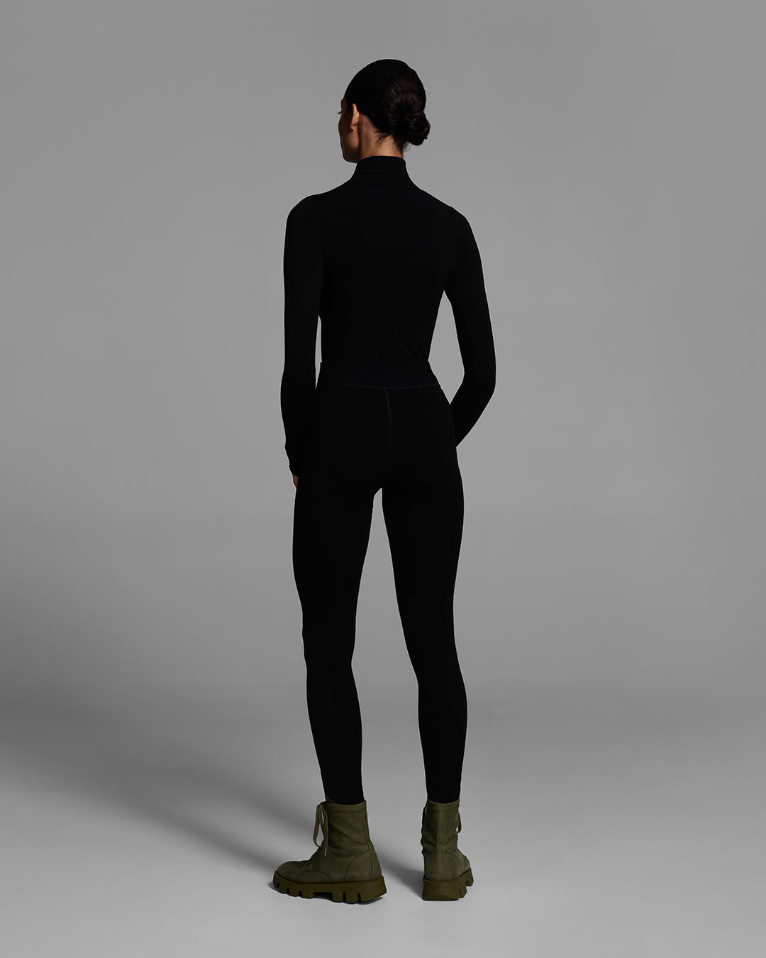 Back view of a woman wearing a black turtleneck and matching pant base layer set made of merino wool blend. #color_onyx