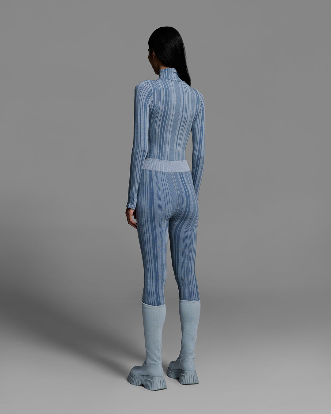 Back view of a woman wearing a slate blue color turtleneck and matching pant base layer set made of merino wool blend. #color_slate