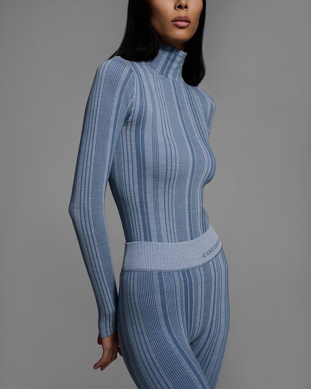 Detail view of a woman wearing a slate blue color turtleneck and matching pant base layer set made of merino wool blend. #color_slate