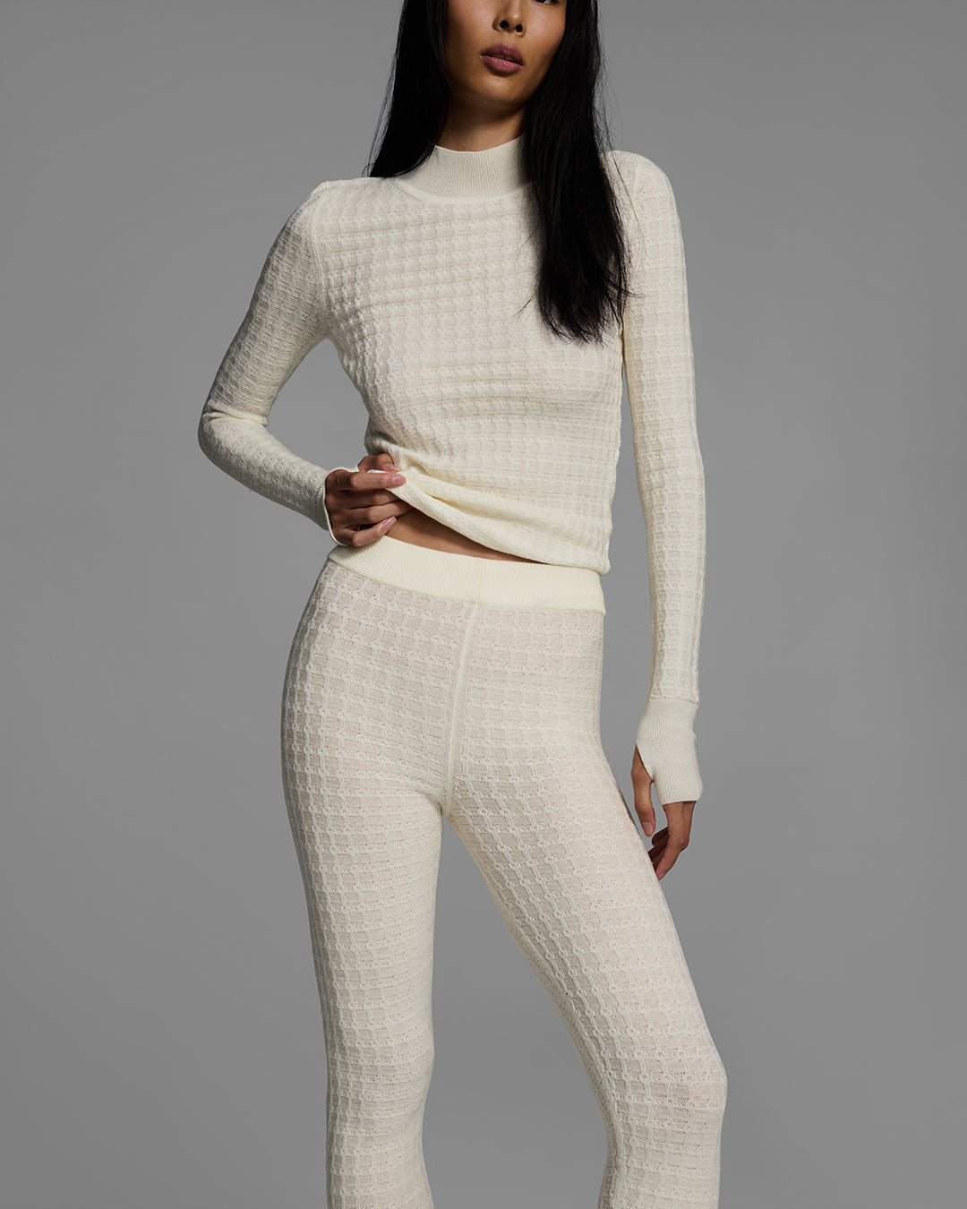 Woman wearing a textural knit base layer top and bottom in off-white with hand adjusting shirt. #color_alabaster