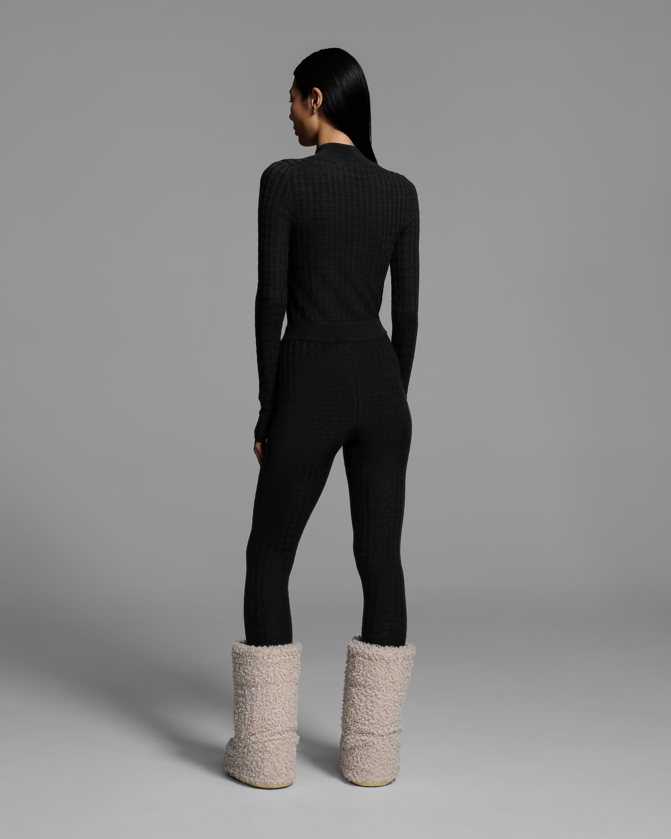 Back view of a woman wearing a textural knit base layer top and bottom in black. #color_onyx