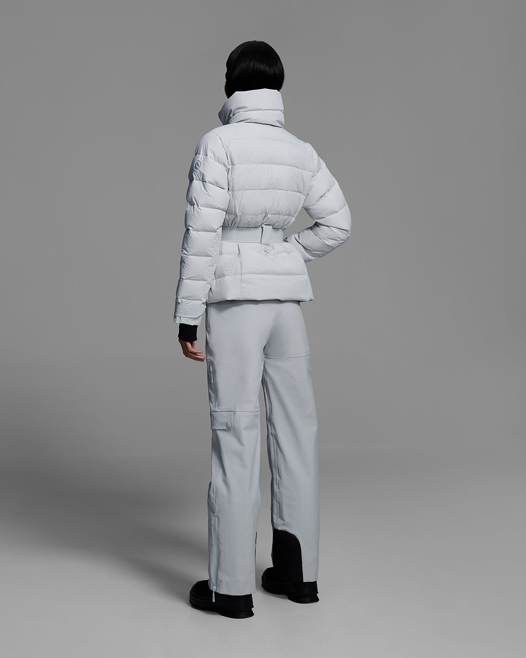 Back view of a woman wearing a belted down-fill puffer ski jacket in smoke gray with matching pant. #color_smoke