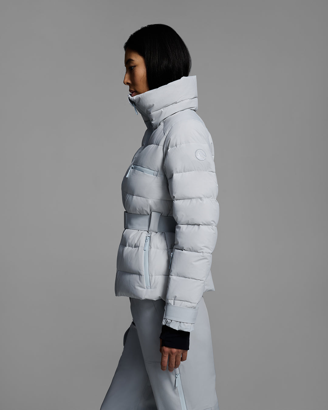 Side view of a woman wearing a belted down-fill puffer ski jacket in smoke gray with matching pant. #color_smoke