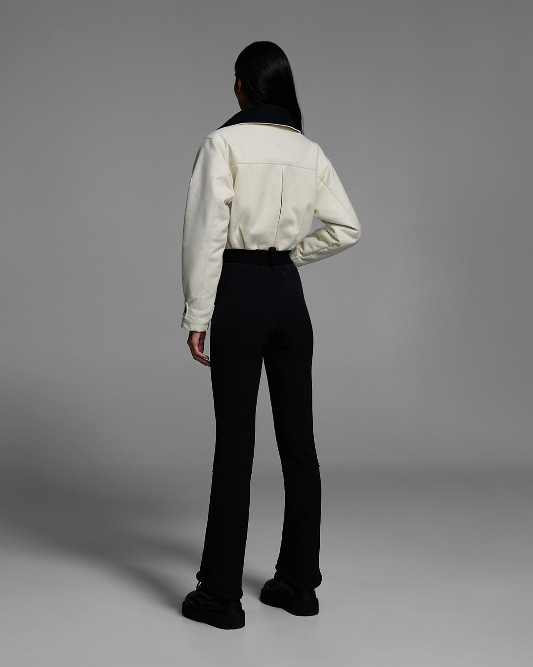 Back view of a woman wearing a natural white color wool top ski suit with belted waist and black 4-way stretch bottom. #color_natural / onyx
