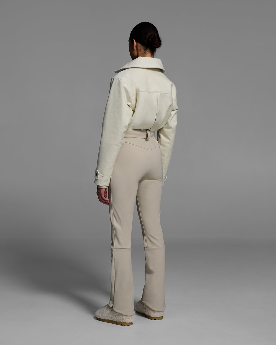 Back view of a woman wearing a natural white color wool top ski suit with belted waist and tan color 4-way stretch bottom. #color_natural / sand