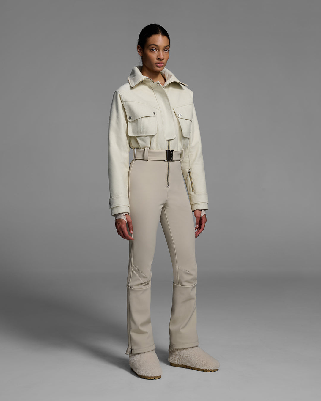 Woman wearing a natural white color wool top ski suit with belted waist and tan color 4-way stretch bottom. #color_natural / sand