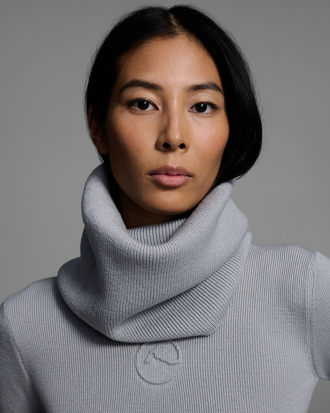 Close up of a woman wearing a gray melange ski buff made of merino wool with matching sweater. #color_gray melange