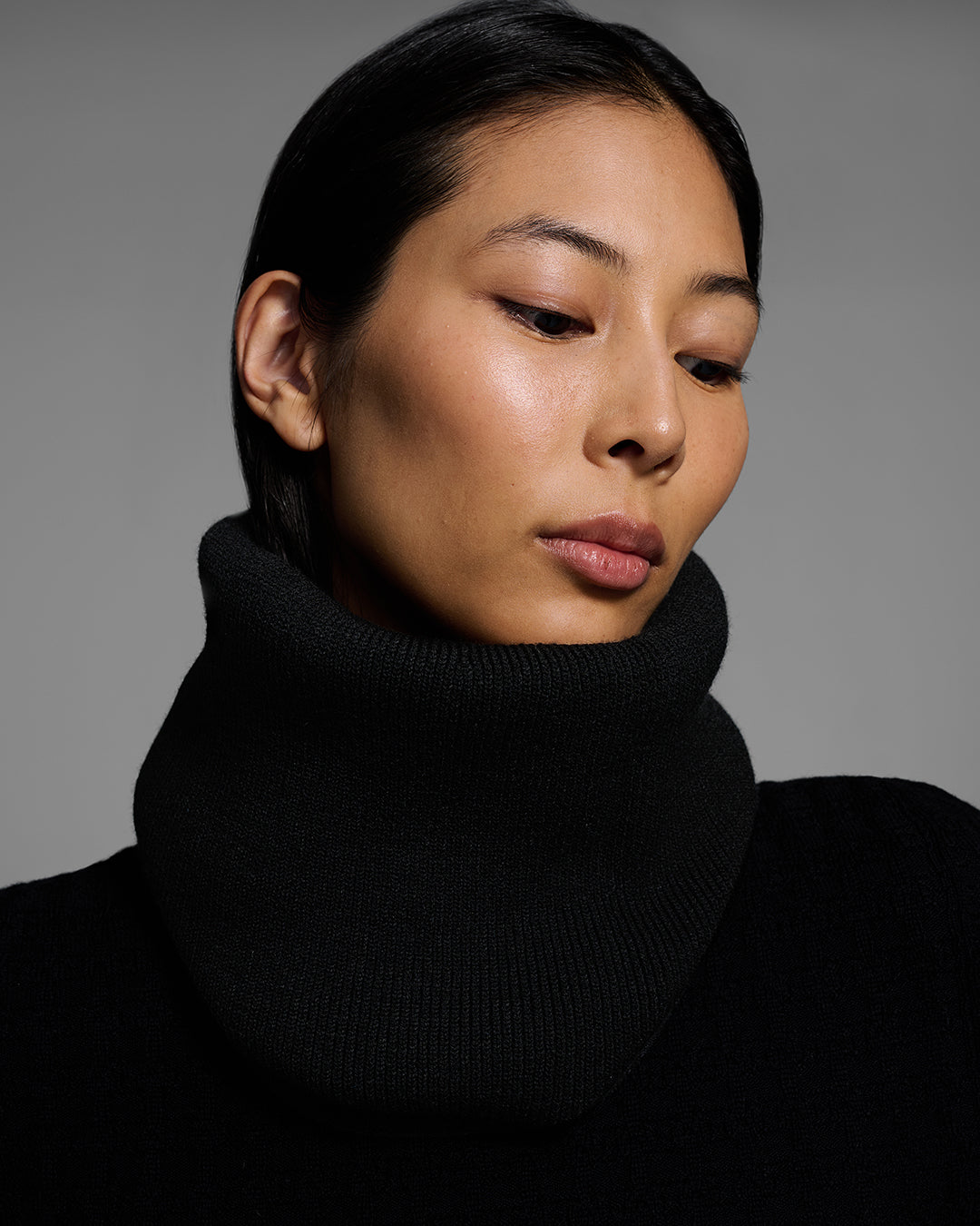 Close up of a woman wearing a black ski buff made of merino wool with matching base layer top. #color_onyx