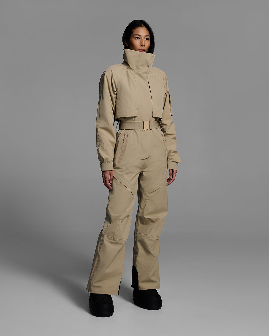 Woman wearing a tan color waterproof technical fabric ski suit with a belted waist. #color_sand