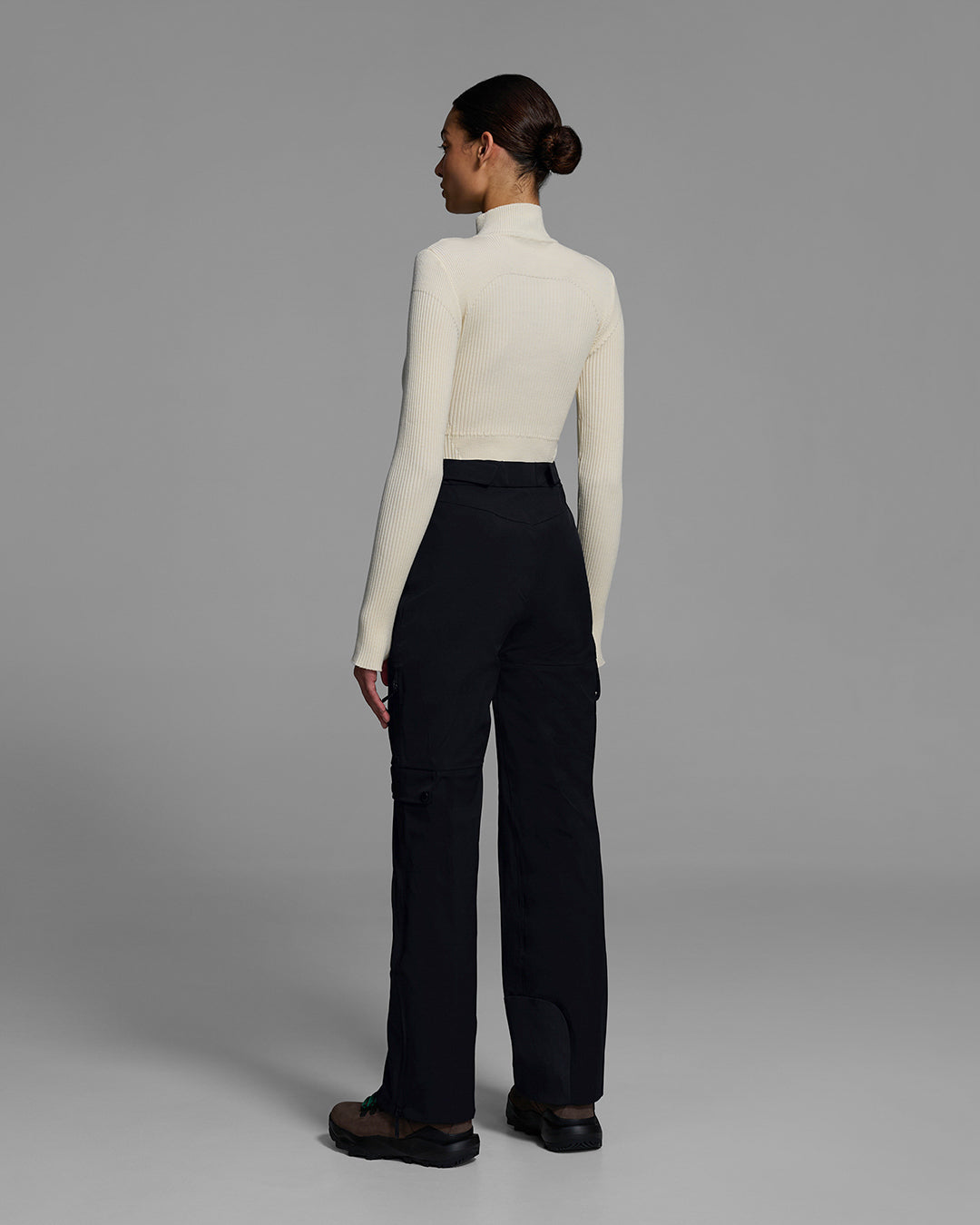Back view of a woman wearing technical ski pants in black with white ski sweater top. #color_onyx