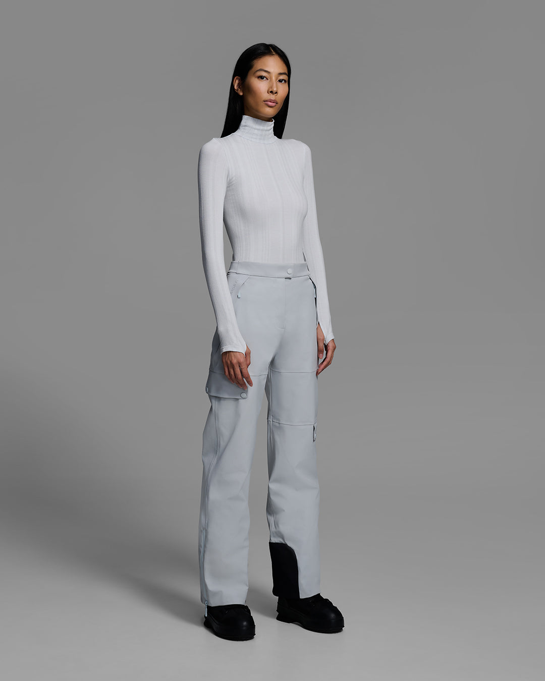 Woman wearing technical ski pants in smoke gray with matching base layer top. #color_smoke