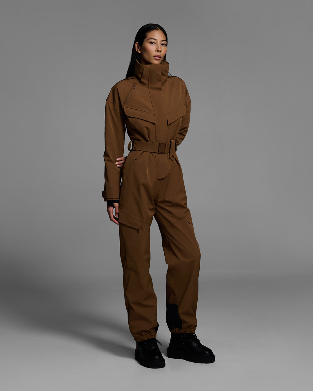 Female model wearing a belted smoke gray color ski suit made of technical waterproof fabric and zippers. #color_sepia