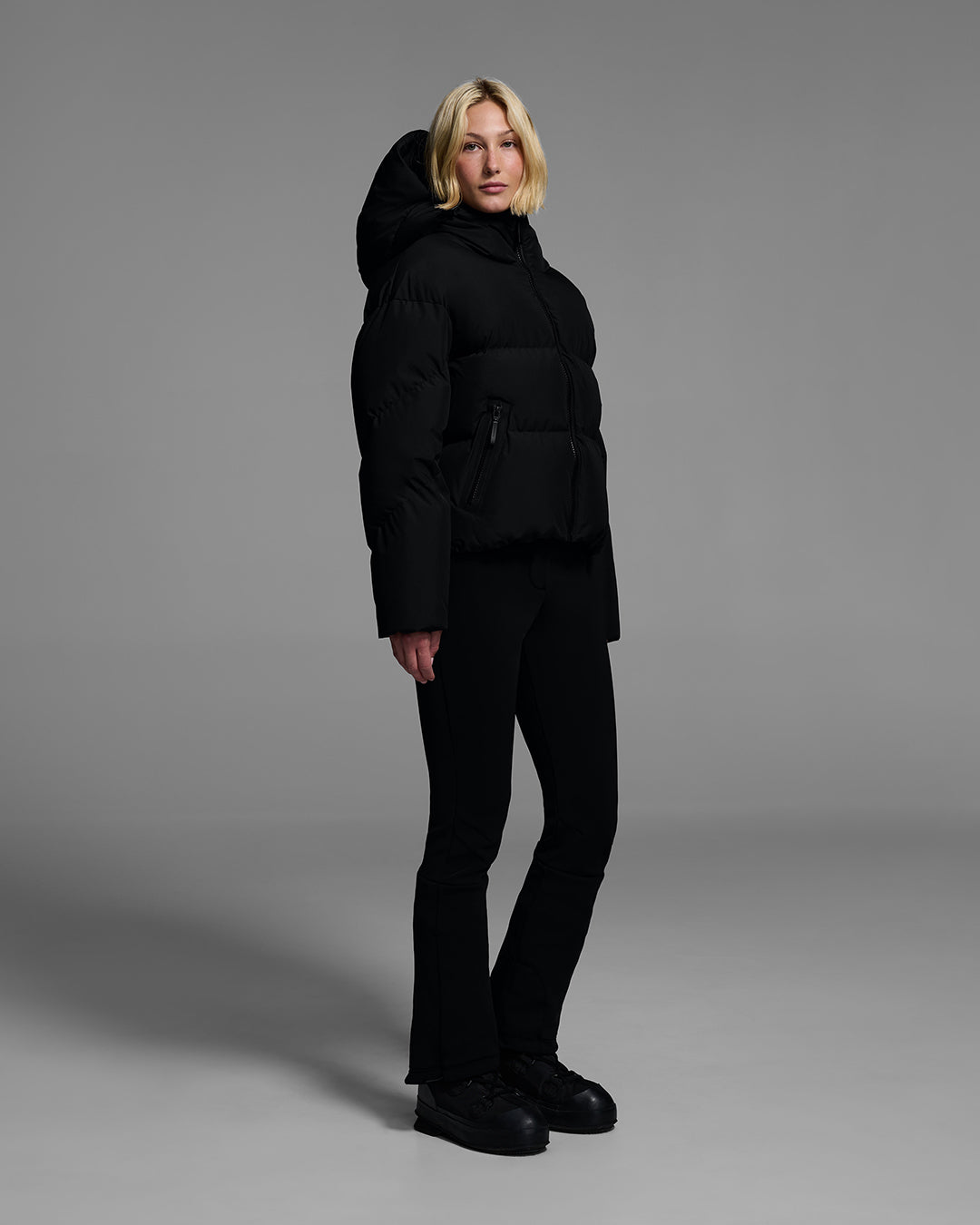 Female model wearing a classic down filled ski jacket in black with a matching ski pant. #color_onyx