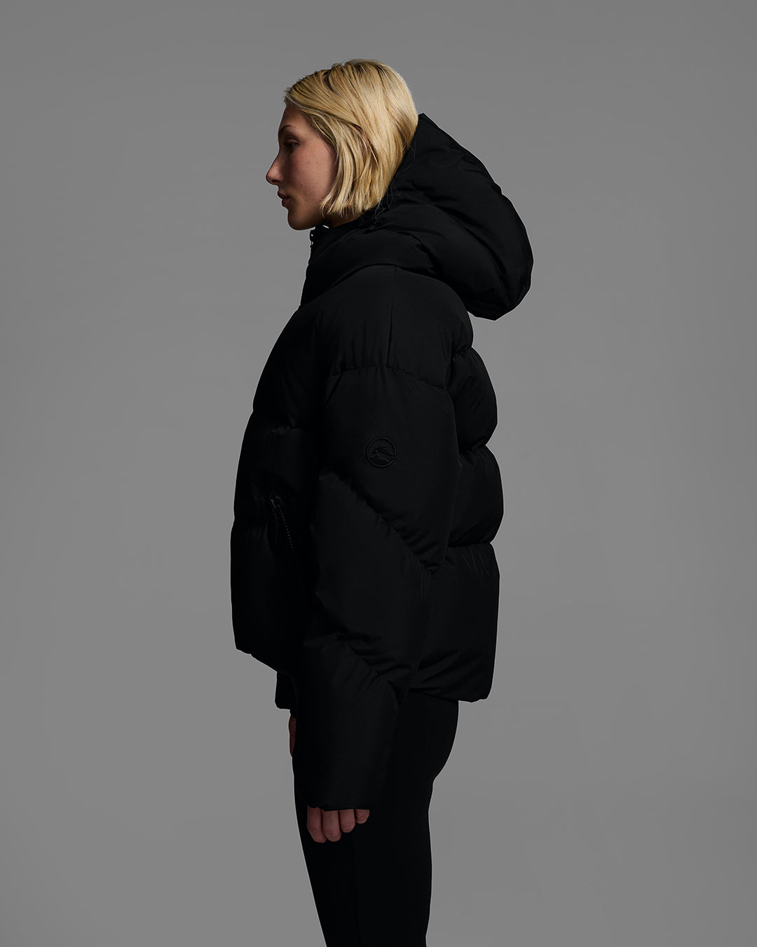 Side view knee up detail shot of a female model wearing a classic down filled ski jacket in black with a matching ski pant. #color_onyx