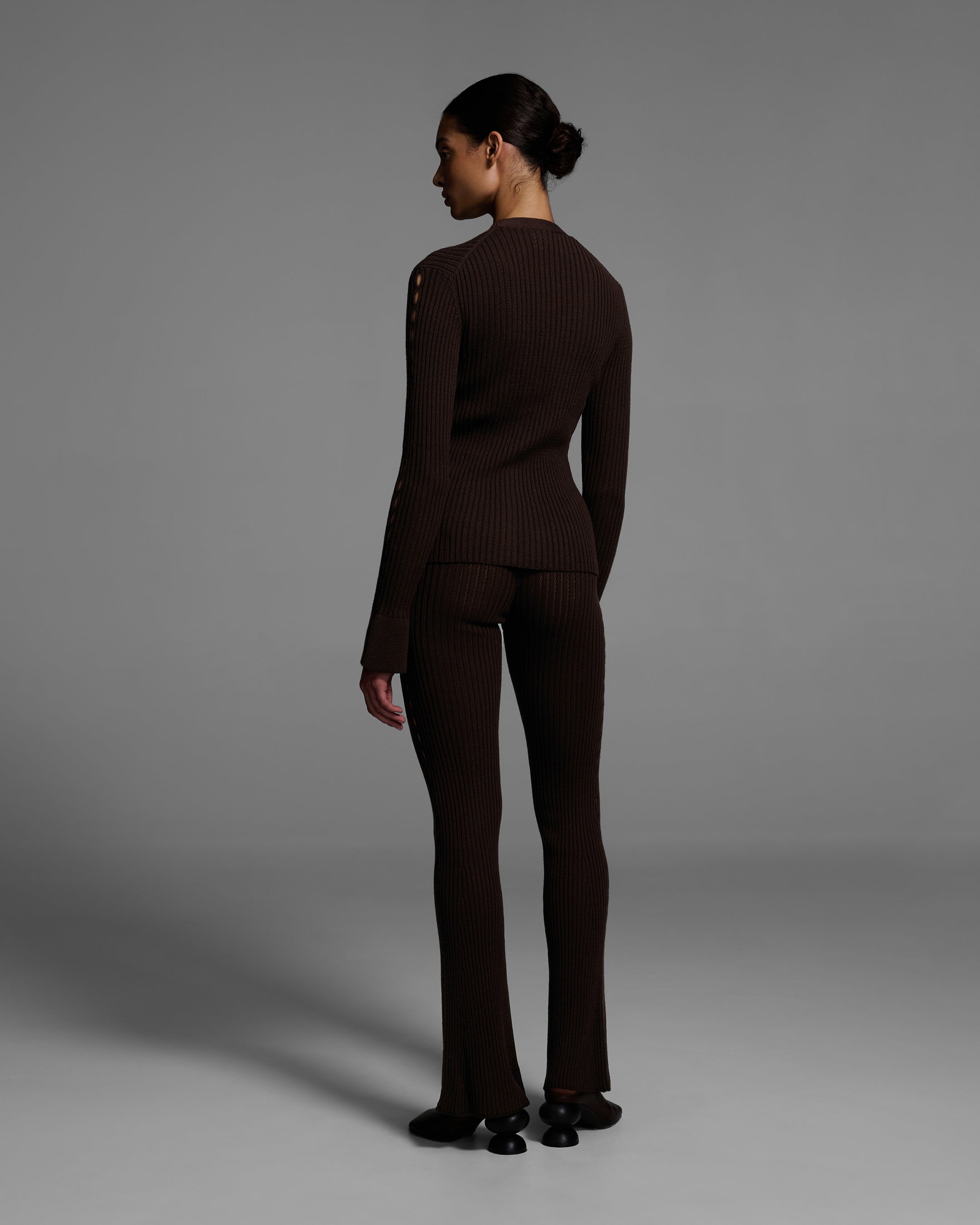 Back view of a woman wearing a chocolate brown knit sweater set with keyholes down the side of arms and legs. #color_chocolate
