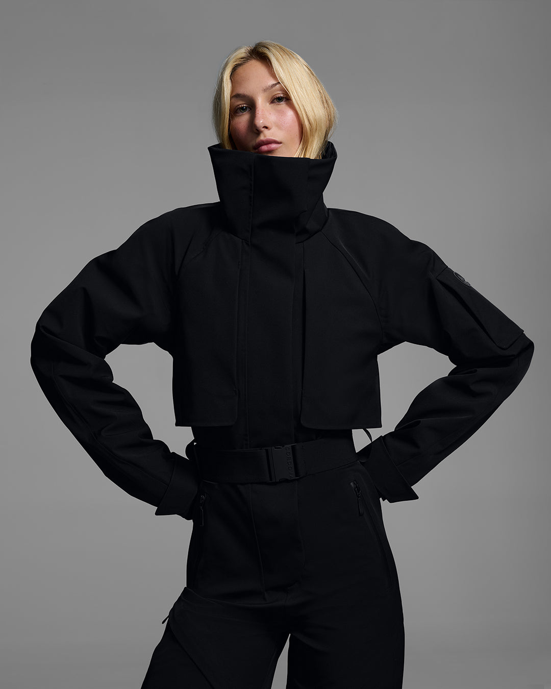 Upper body detail view of a woman wearing a black color waterproof technical fabric ski suit with a belted waist. #color_onyx