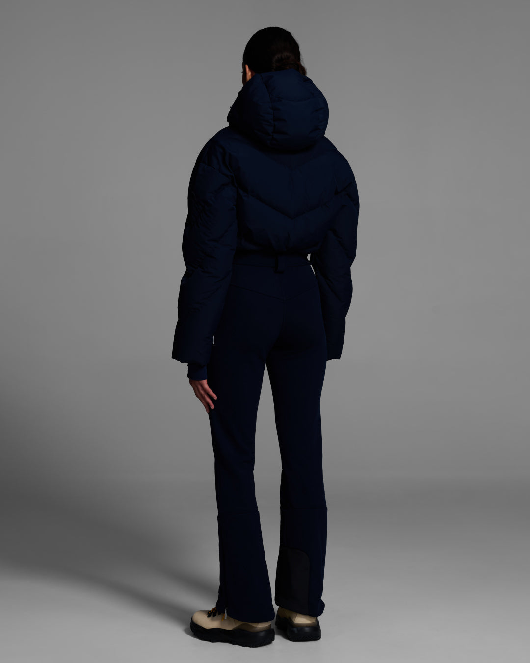 Back view of female model with wearing a belted indigo blue color ski suit with down filled top and 4-way stretch bottom. #color_indigo