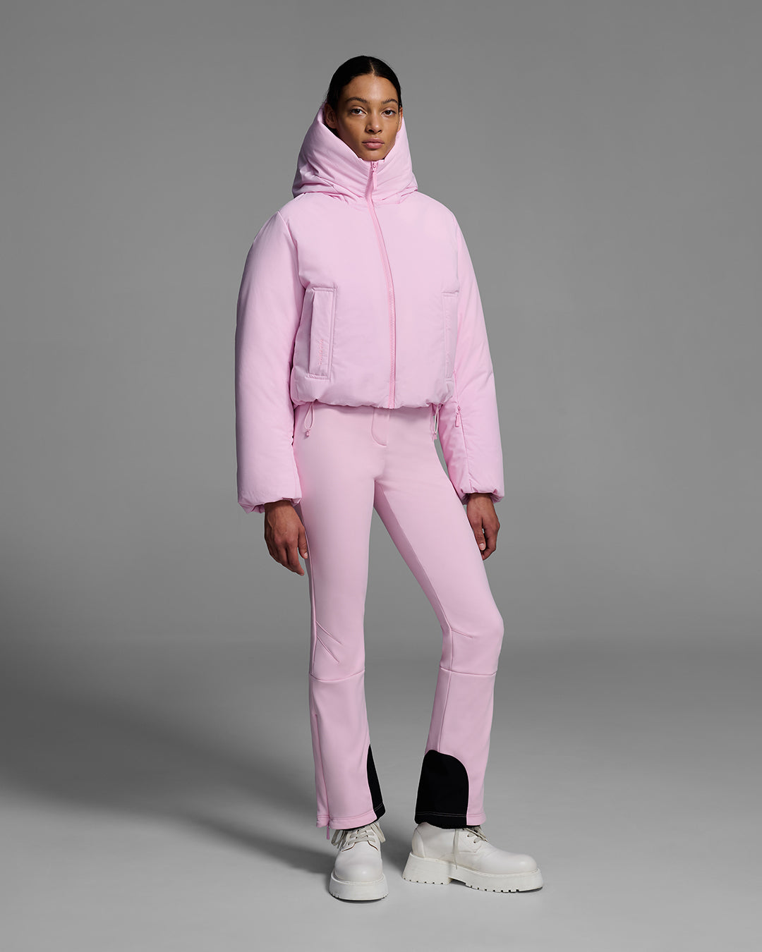 Female model wearing a down filled ski jacket in peony pink fabric, zipped up with a matching pink ski pant. #color_peony