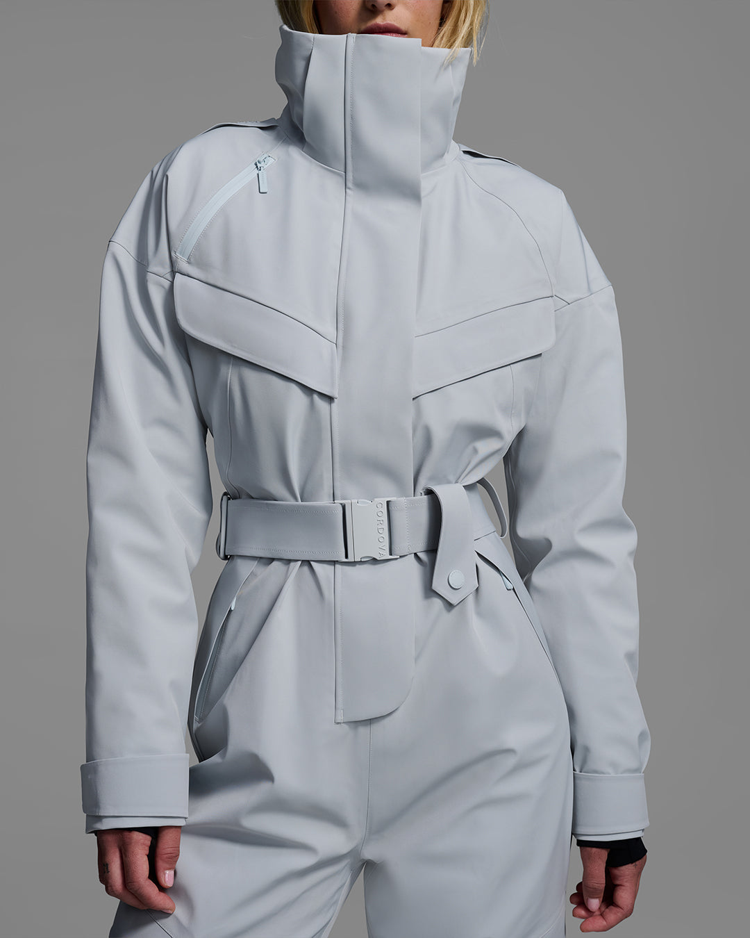 Detail view of a female model wearing a belted smoke gray color ski suit made of technical waterproof fabric and zippers. #color_smoke