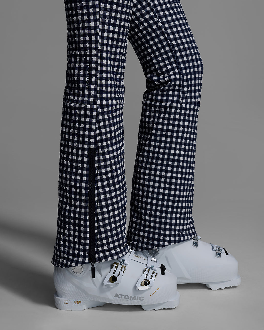 Detail view of the leg and boot gaiter of a female model wearing an indigo blue and white gingham print ski suit #color_indigo gingham