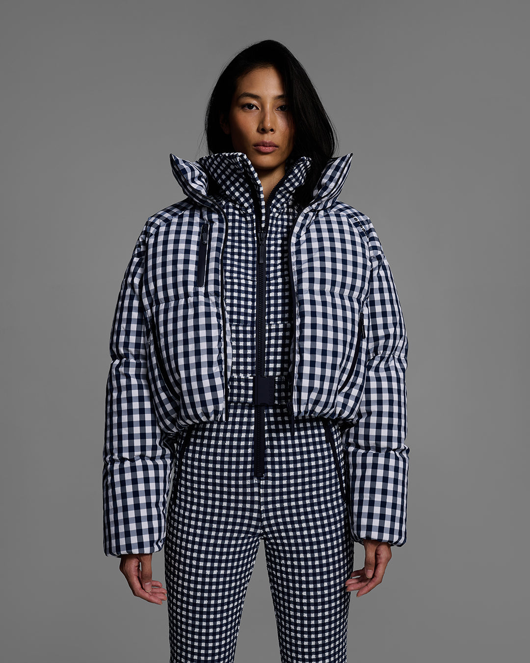 Detail view of a female model wearing a belted indigo blue and white gingham print ski suit with matching down jacket o top. #color_indigo gingham