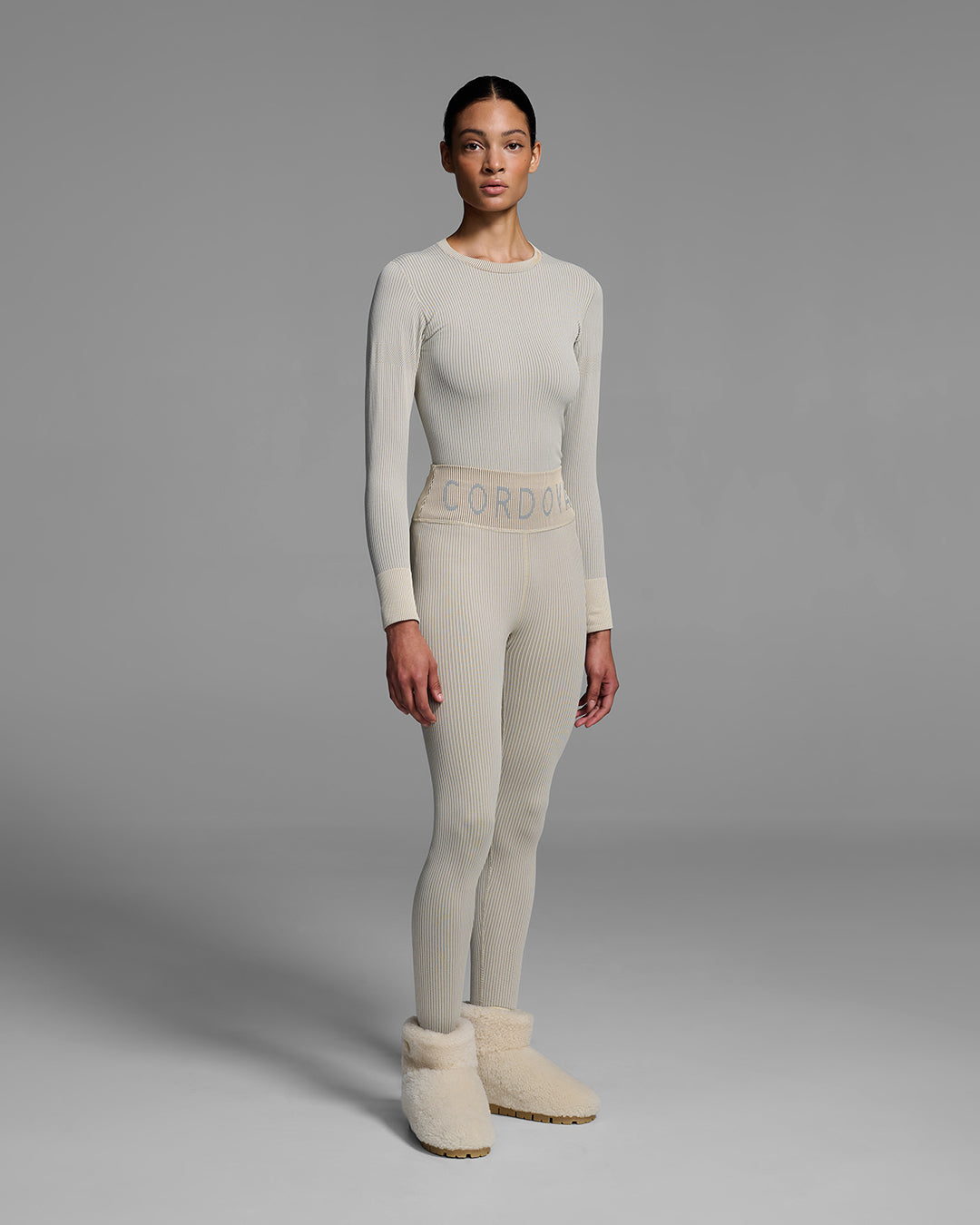 Female model wearing a matching ski base layer set in a compression knit fabric and ecru tan color. #color_ecru