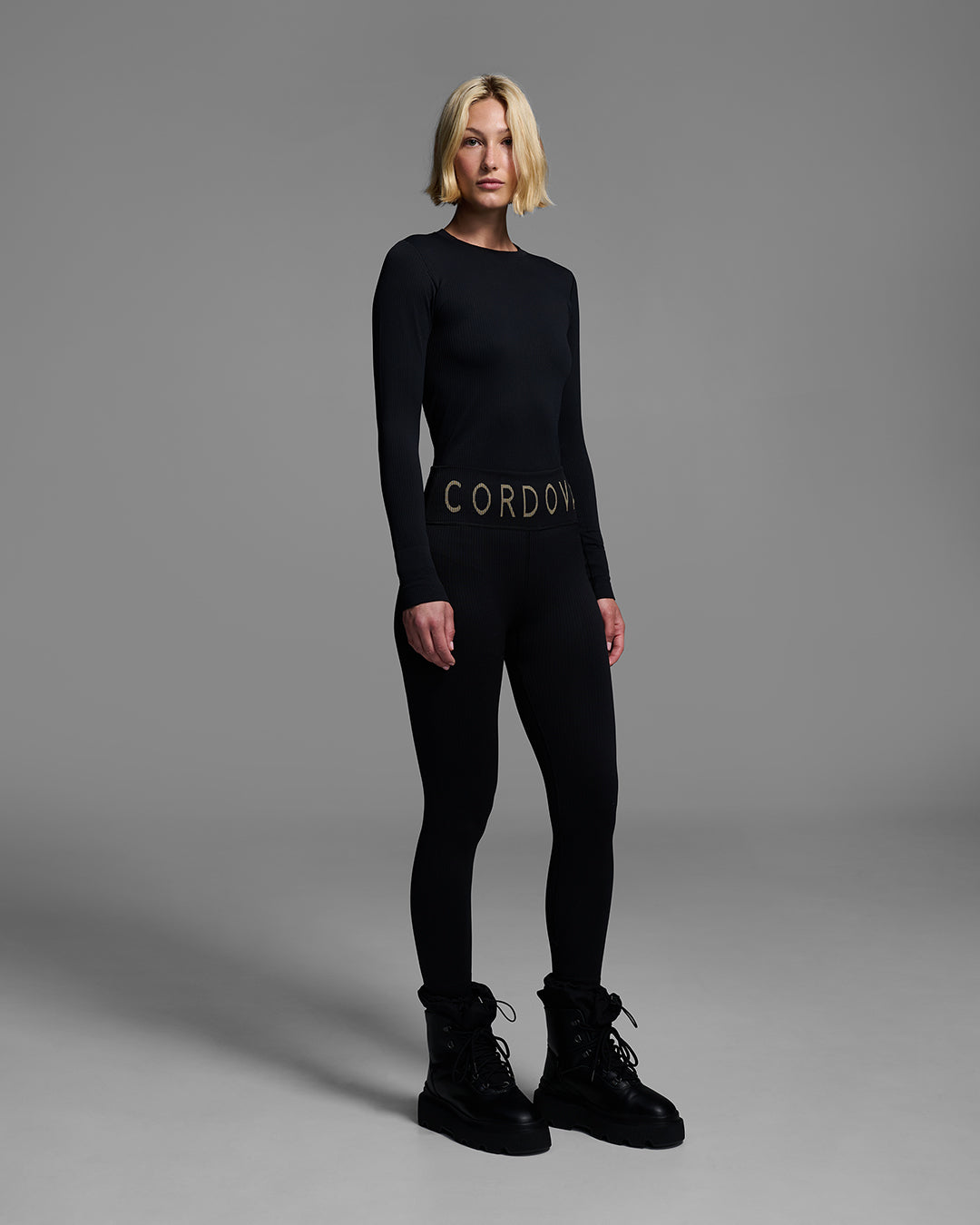 Female model wearing a matching ski base layer set in a compression knit fabric and onyx black color. #color_onyx