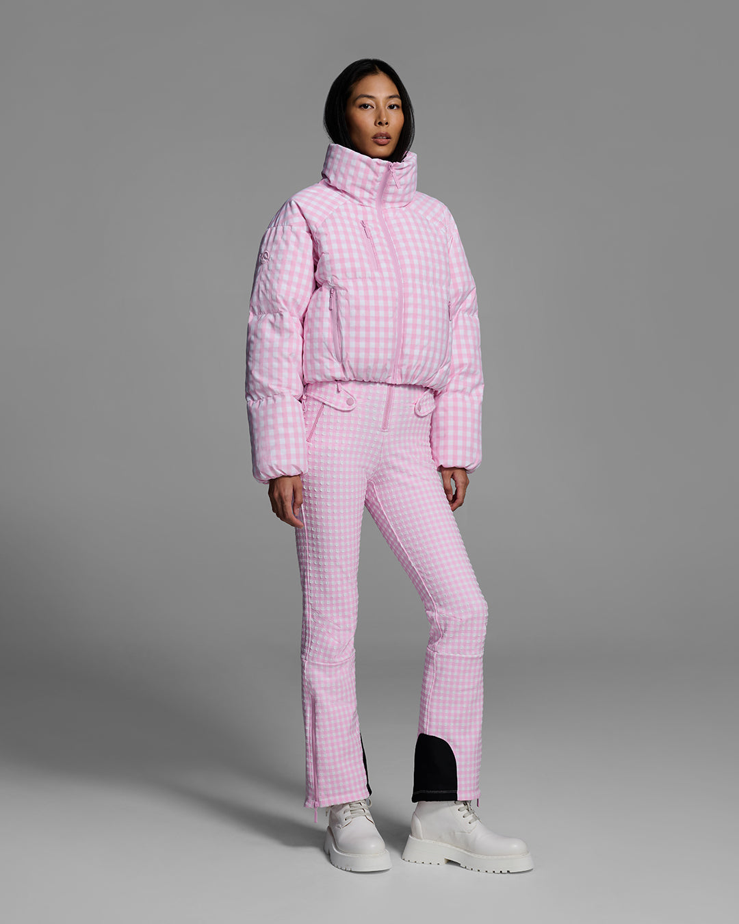 Female model wearing a down filled ski jacket in peony pink gingham fabric with matching ski suit underneath. #color_peony gingham