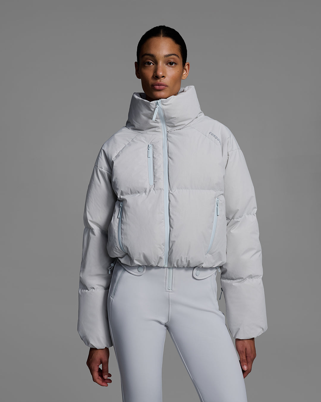 Female model wearing a down filled ski jacket in smoke gray fabric  with a matching ski bib underneath. #color_smoke