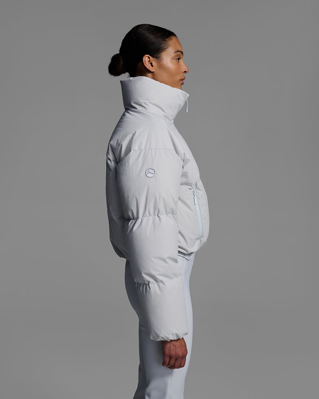 Side view of a female model wearing a down filled ski jacket in smoke gray fabric  with a matching ski bib underneath. #color_smoke