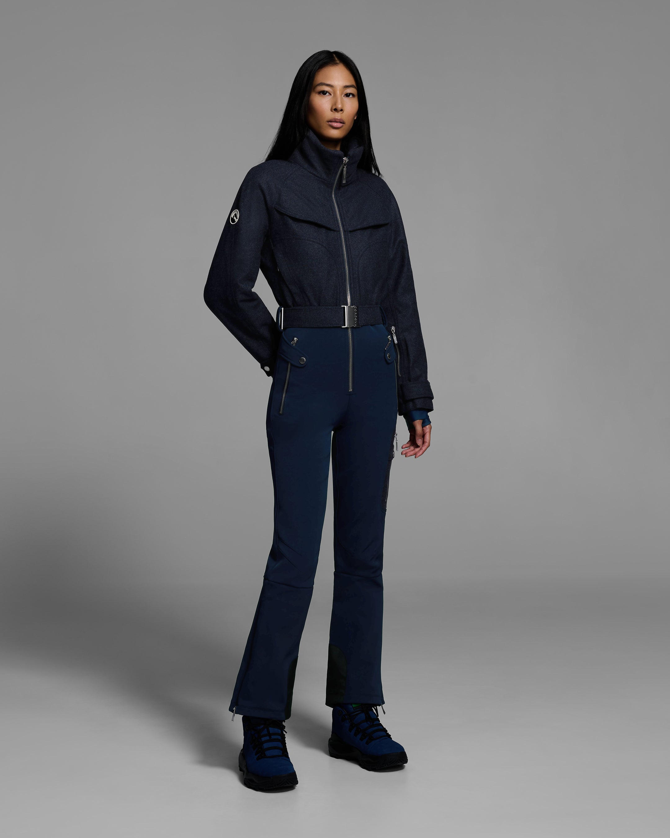 Female model wearing a belted indigo denim melange ski suit with a wool top and 4-way stretch water-resistant fabric bottom. #color_indigo