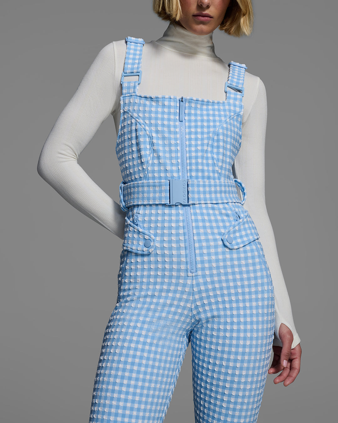Torso detail view of a female model wearing a belted cerulean blue color ski bib in a gingham print. #color_cerulean gingham