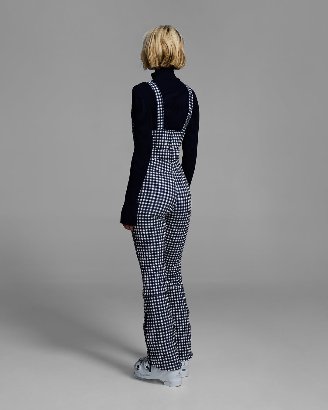 Back view of a female model wearing a belted indigo blue color ski bib in a gingham print. #color_indigo gingham