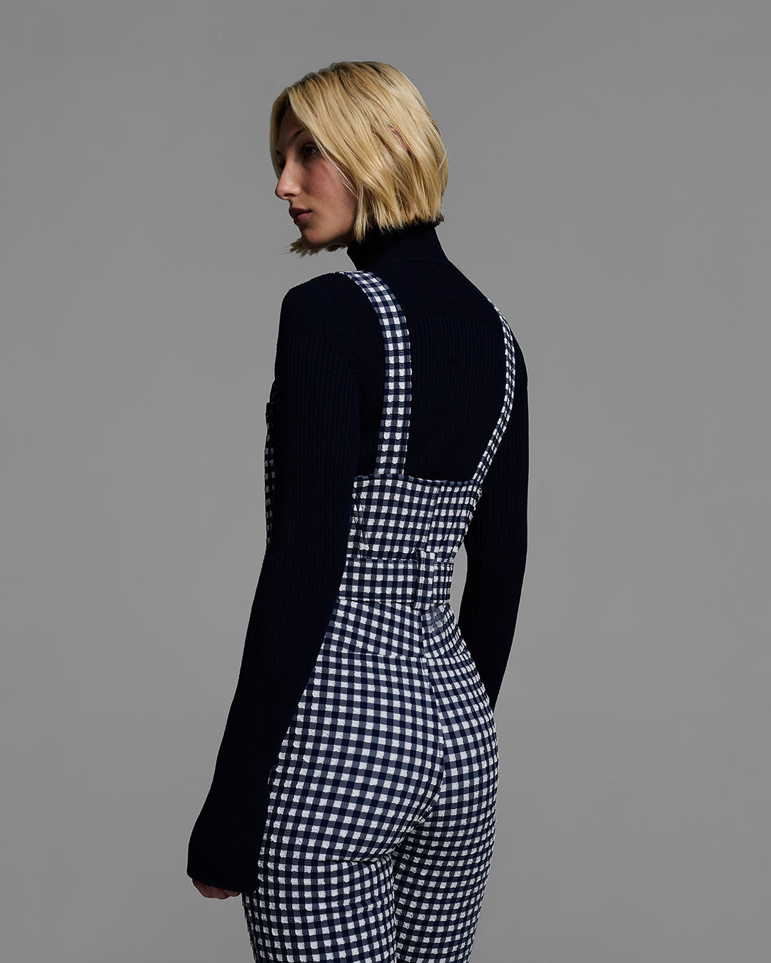 Back detail view of a female model wearing a belted indigo blue color ski bib in a gingham print. #color_indigo gingham