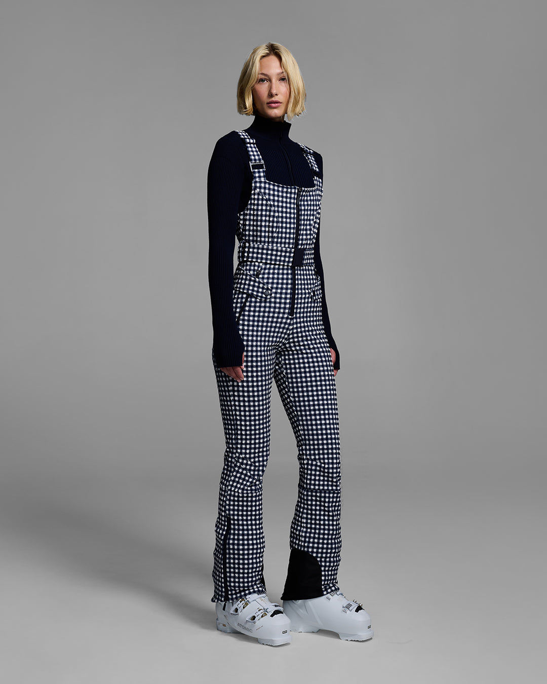 Female model wearing a belted indigo blue color ski bib in a gingham print. #color_indigo gingham