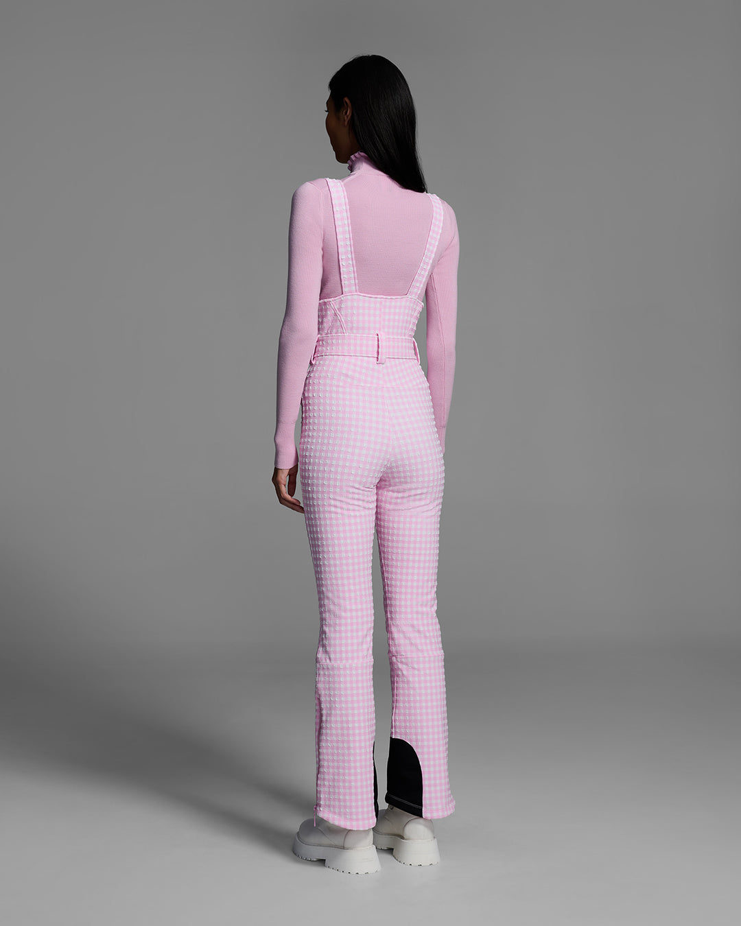 Back view of a female model wearing a belted peony pink color ski bib in a gingham print. #color_peony gingham