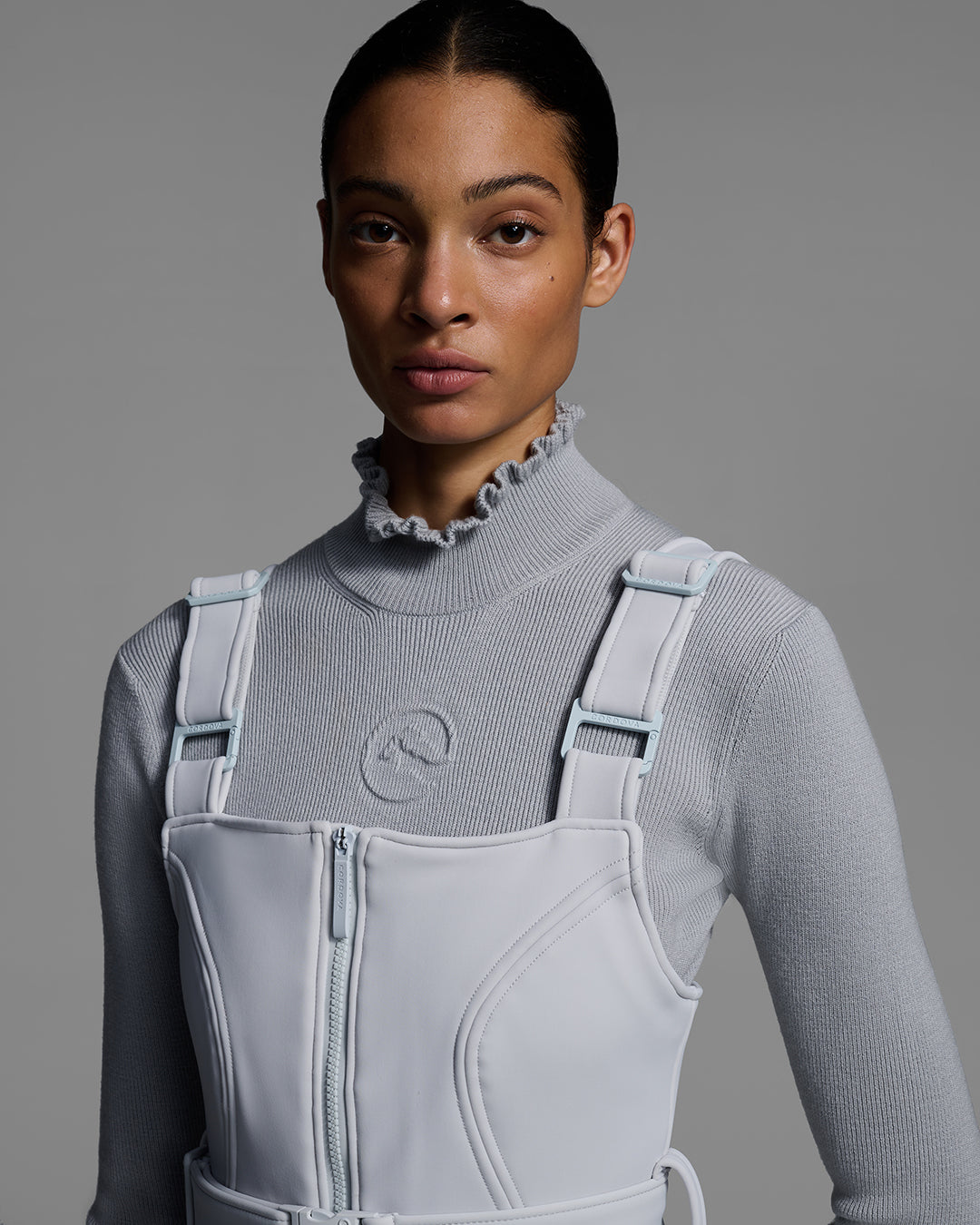 Detail view from waist up of female model wearing a smoke gray color ski bib with a matching gray sweater. #color_smoke
