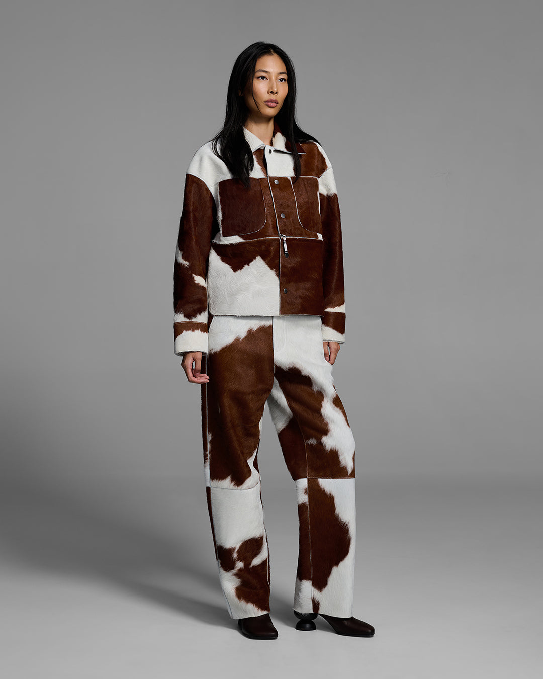 Female model wearing a matching jacket and pant set crafted in hair-on cowhide leather. #color_cowhide