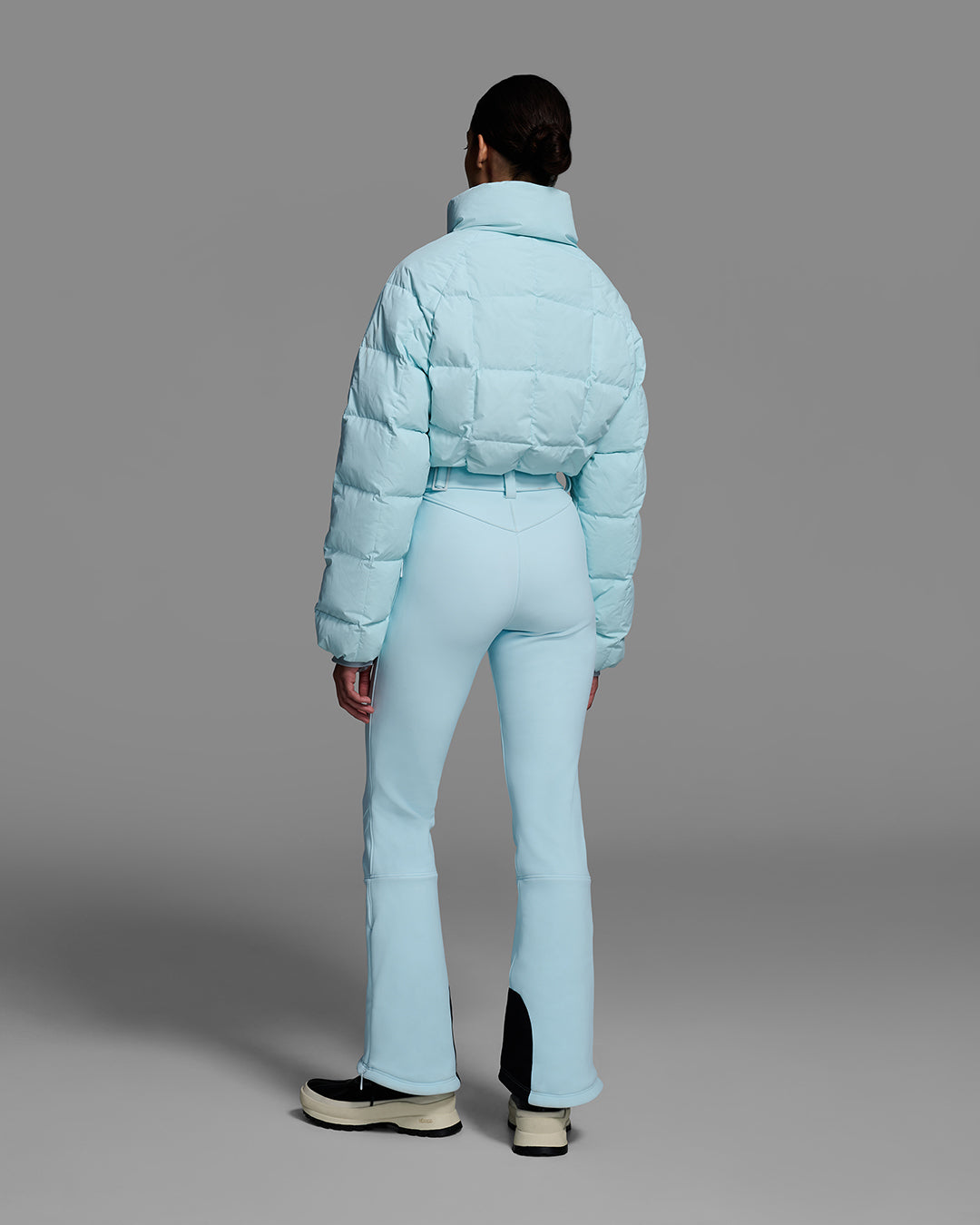 Back view of a woman in an iceberg blue ski suit with a quilted down top, belted waist, and 4-way stretch pant. #color_iceberg