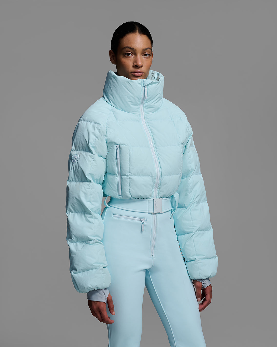 Knee up detail view of a female model wearing a belted iceberg blue color ski suit with quilted, down filled top and 4-way stretch bottom. #color_iceberg