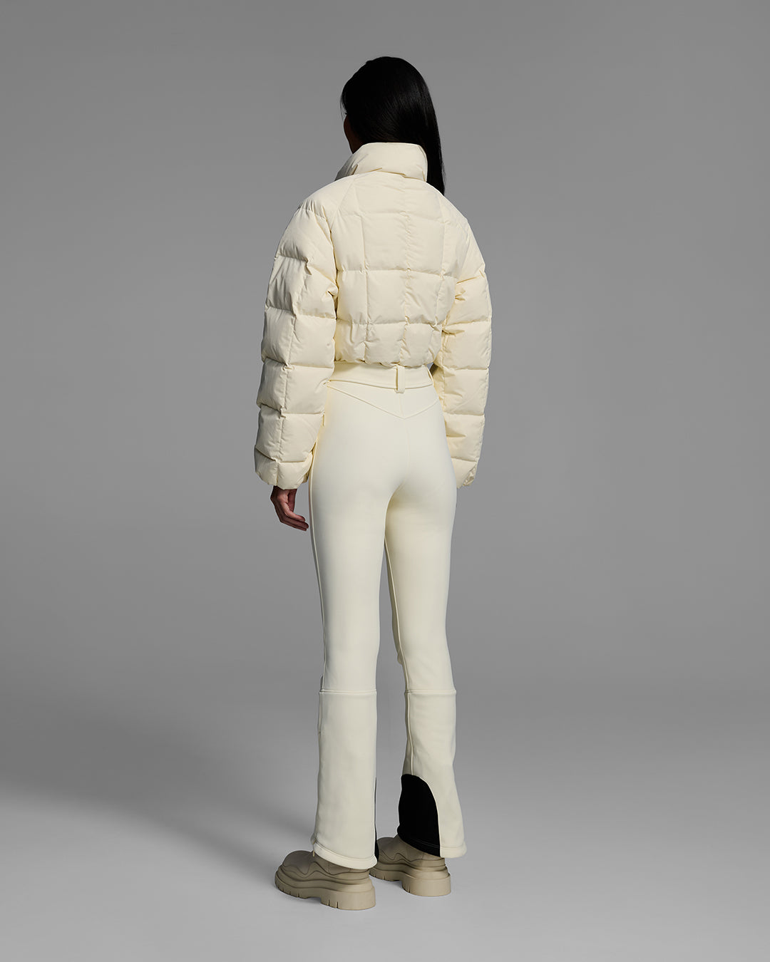 Back view of a female model wearing a belted alabaster white color ski suit with quilted, down filled top and 4-way stretch bottom. #color_alabaster